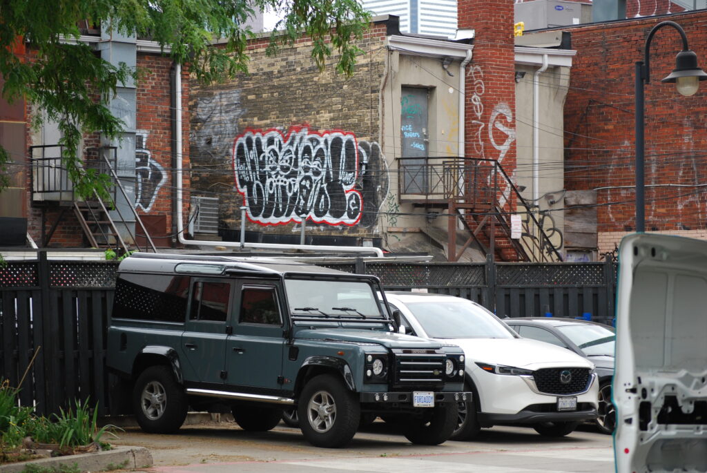 Land Rover gris taupe stationné dans une ruelle de Toronto. Arrière plan de graffitis.