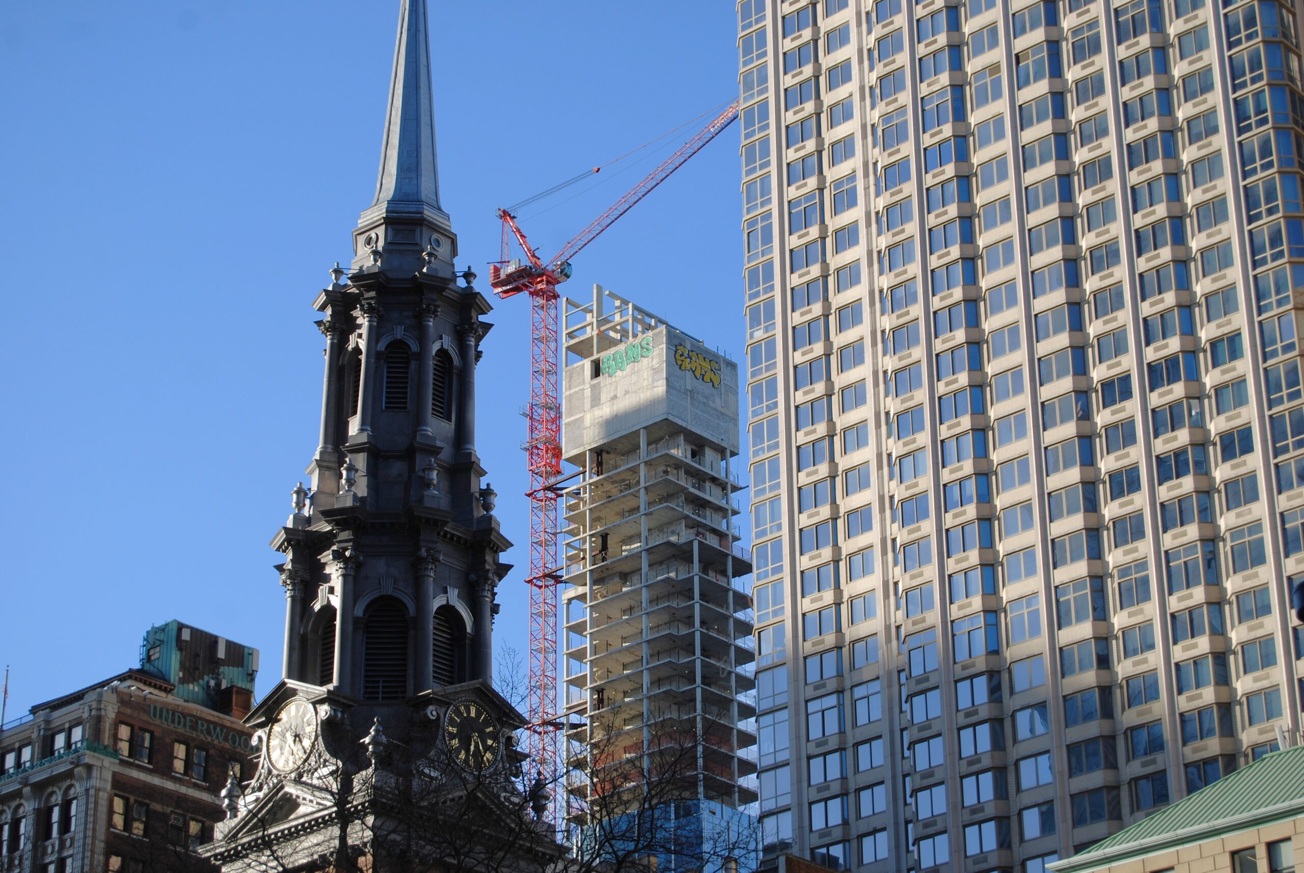 3 éléments à différentes profondeurs: Un clocher d'église à l'avant (gauche), un bâtiment de béton vitré au milieu (droite) et un bâtiment en construction à l'arrière (milieu)