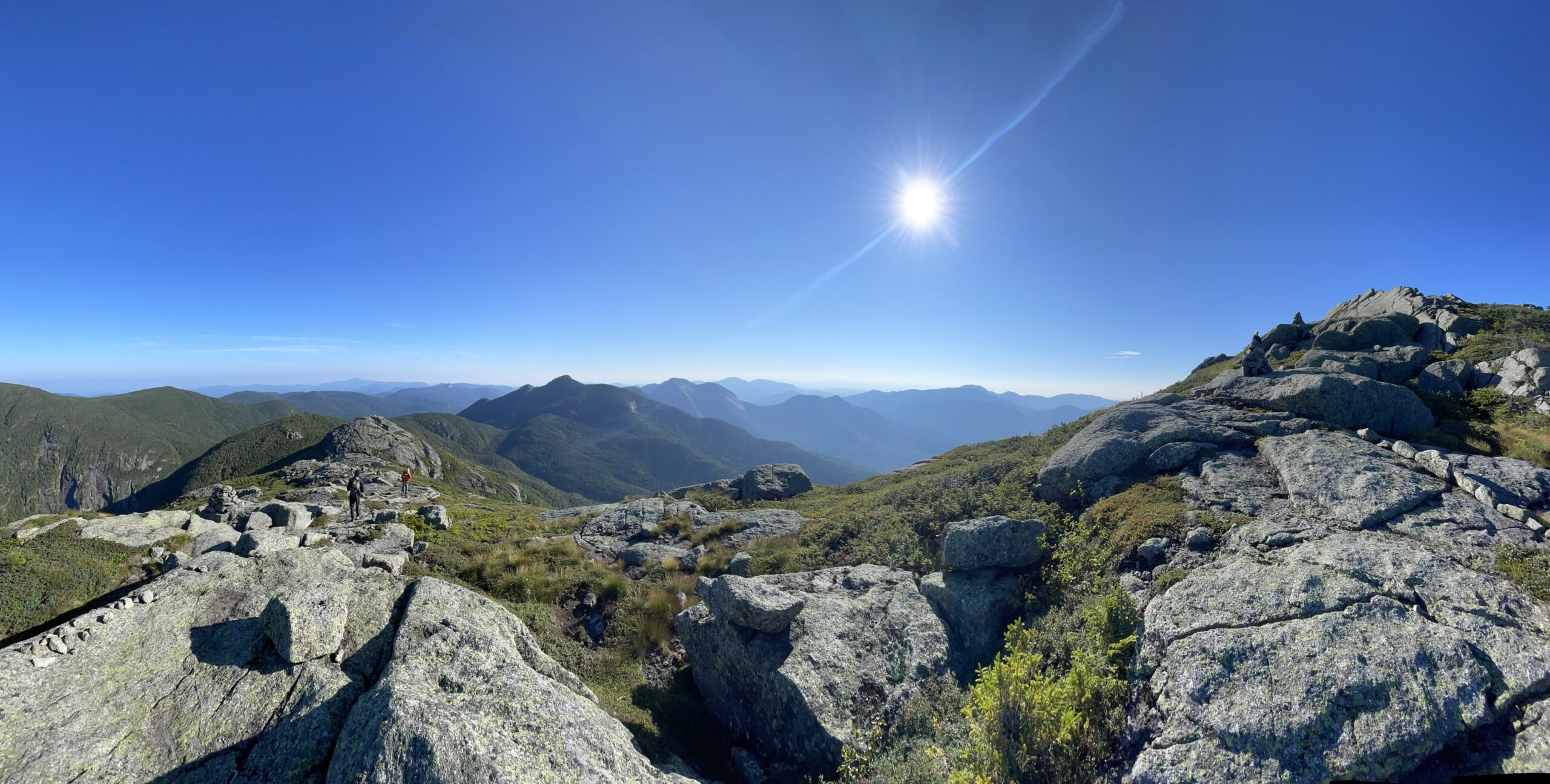 Paysage montagneux, soleil fort, lumière blanche et très claire, soleil bleu, sommet rocheux avec quelques arbustes.
